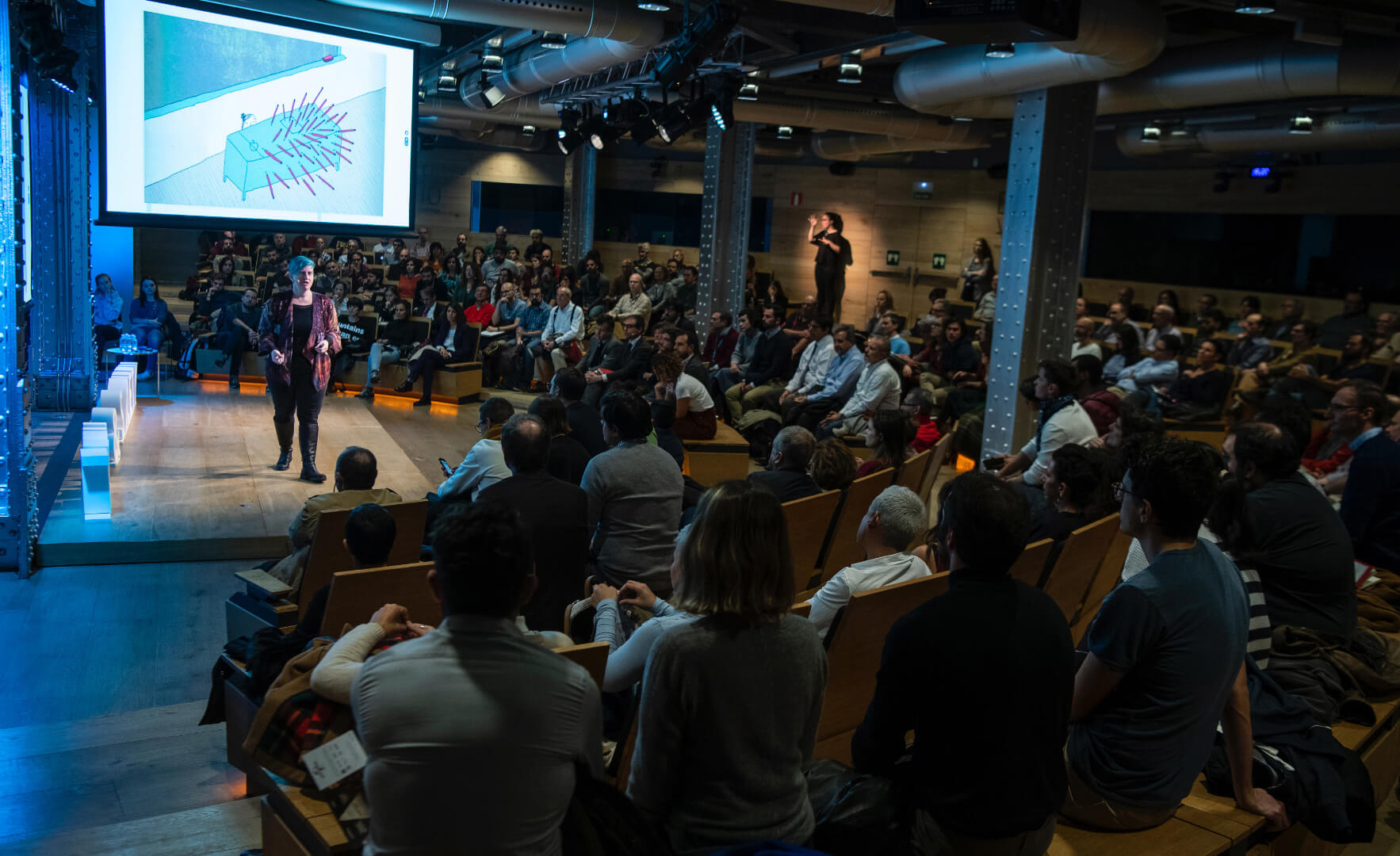 Mujer sobre un escenario dando una charla en un evento tecnológico