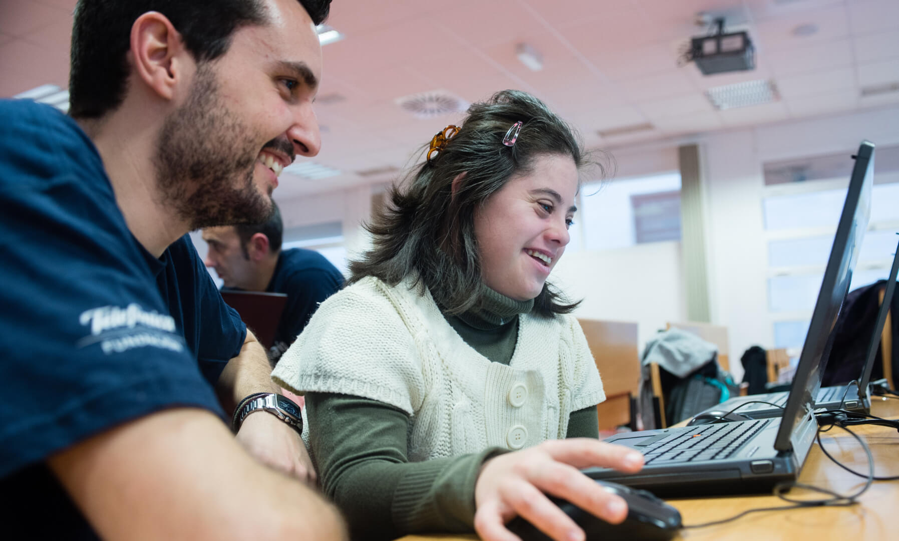 Jóven en una clase de informática con una chica con Síndrome de Down