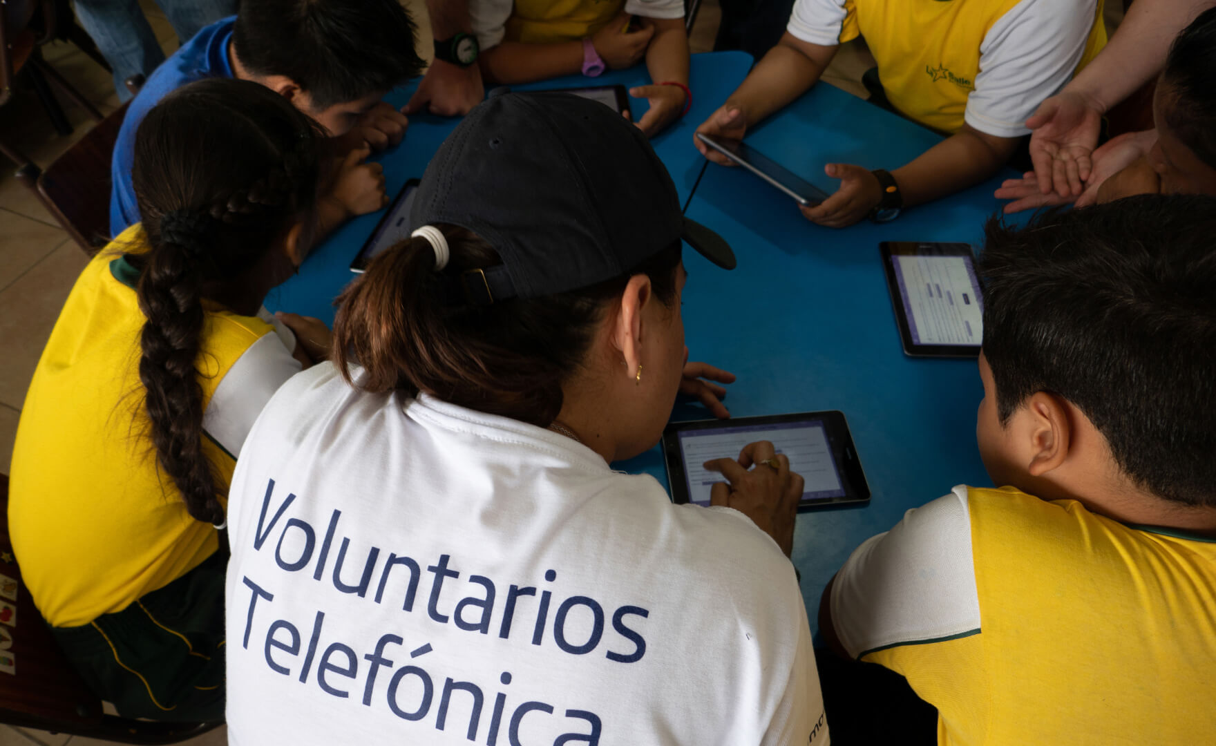 Mujer voluntaria de Telefónica de espaldas sentada en un silla alrededor de niños