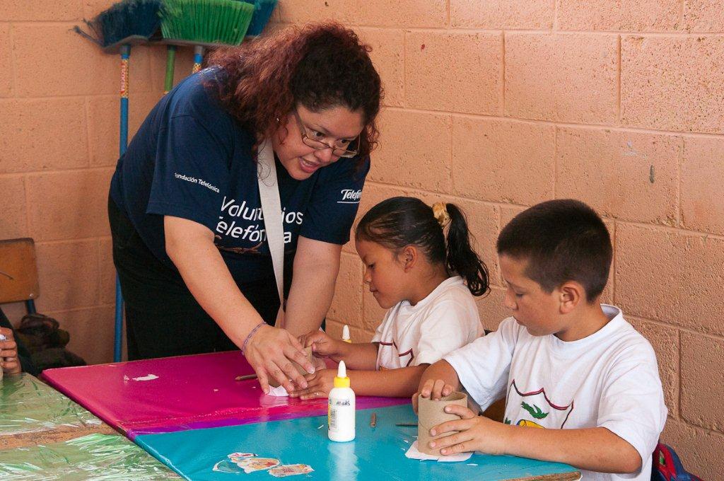 Los Voluntarios Telefónica ayudan a los niños en su trabajo manual.