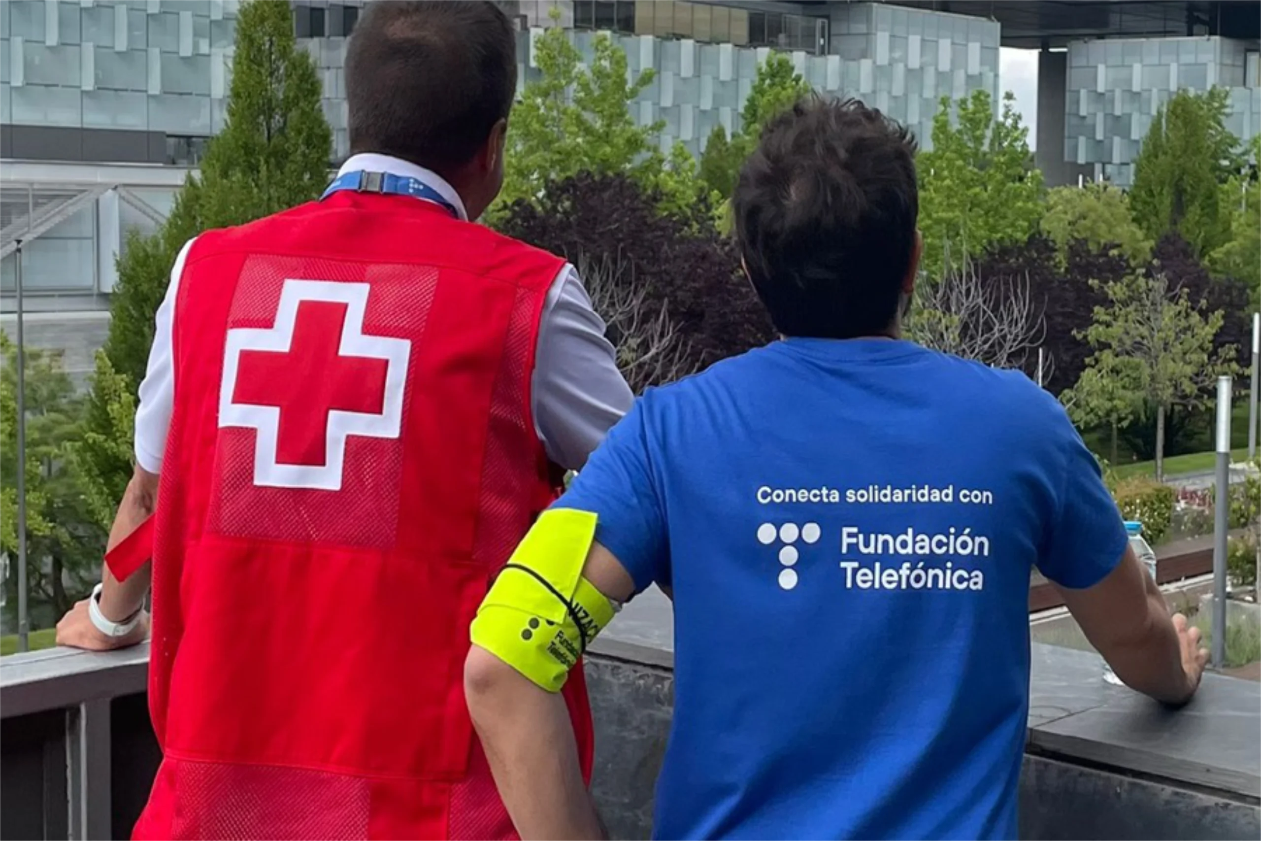 Un trabajador de Cruz Roja y un voluntario de Fundación Telefónica miran de espaldas a un edificio de Distrito Telefónica