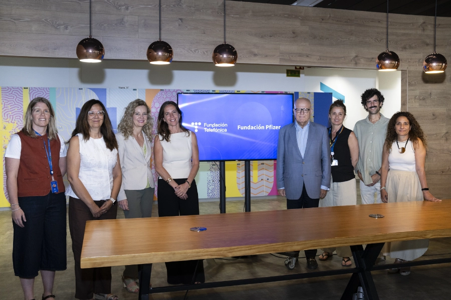 Un momento de la firma entre Fundación Telefónica y Fundación Pfizer para impulsar la salud digital de las personas mayores con Reconectados Salud Digital Group of professionals posing in a modern conference room, with a screen showing Fundación Telefónica and Pfizer logos.
