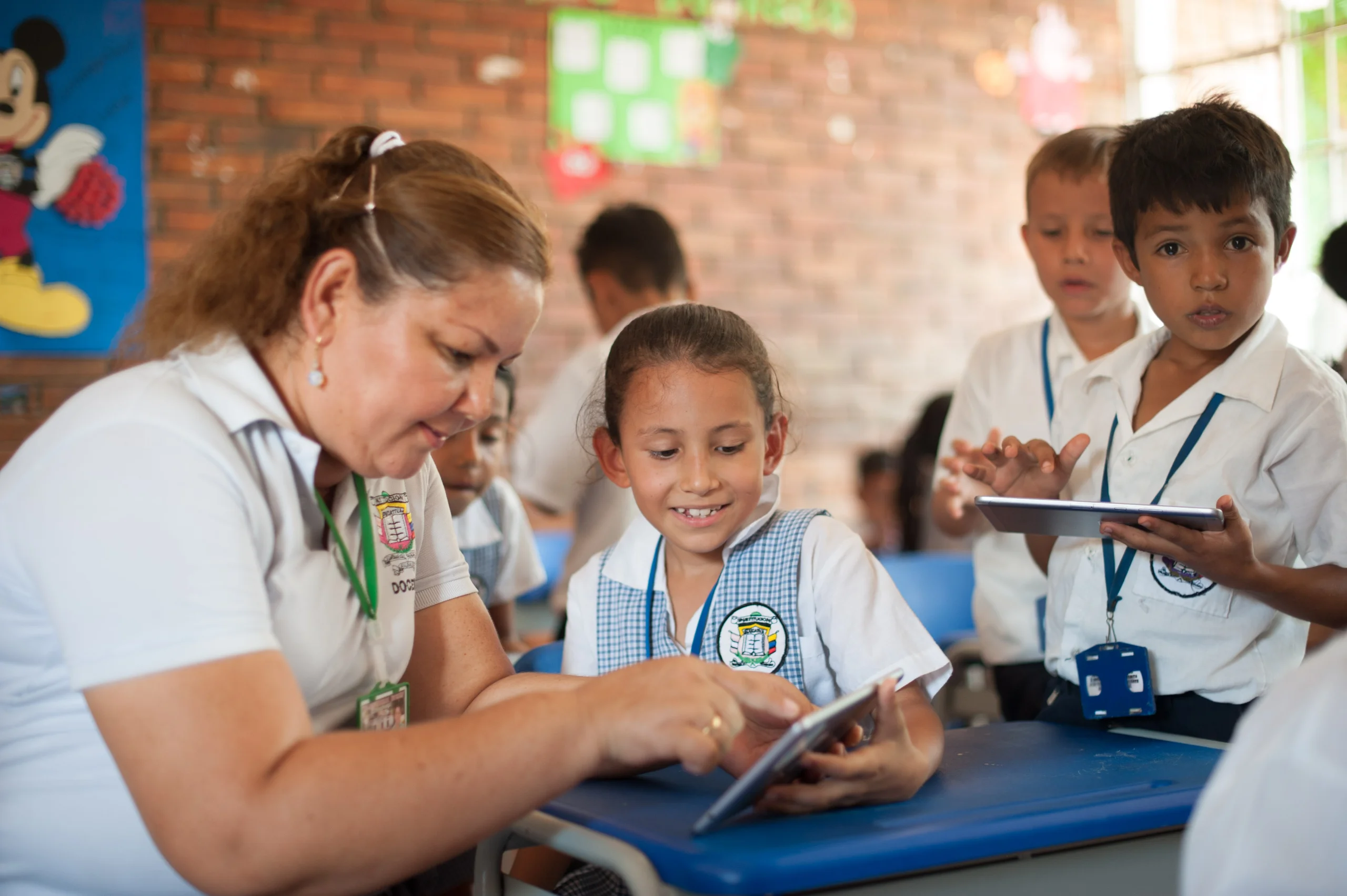 Un grupo de estudiantes miran una tableta digital junto a su profesora Un grupo de estudiantes miran una tableta digital junto a su profesora
